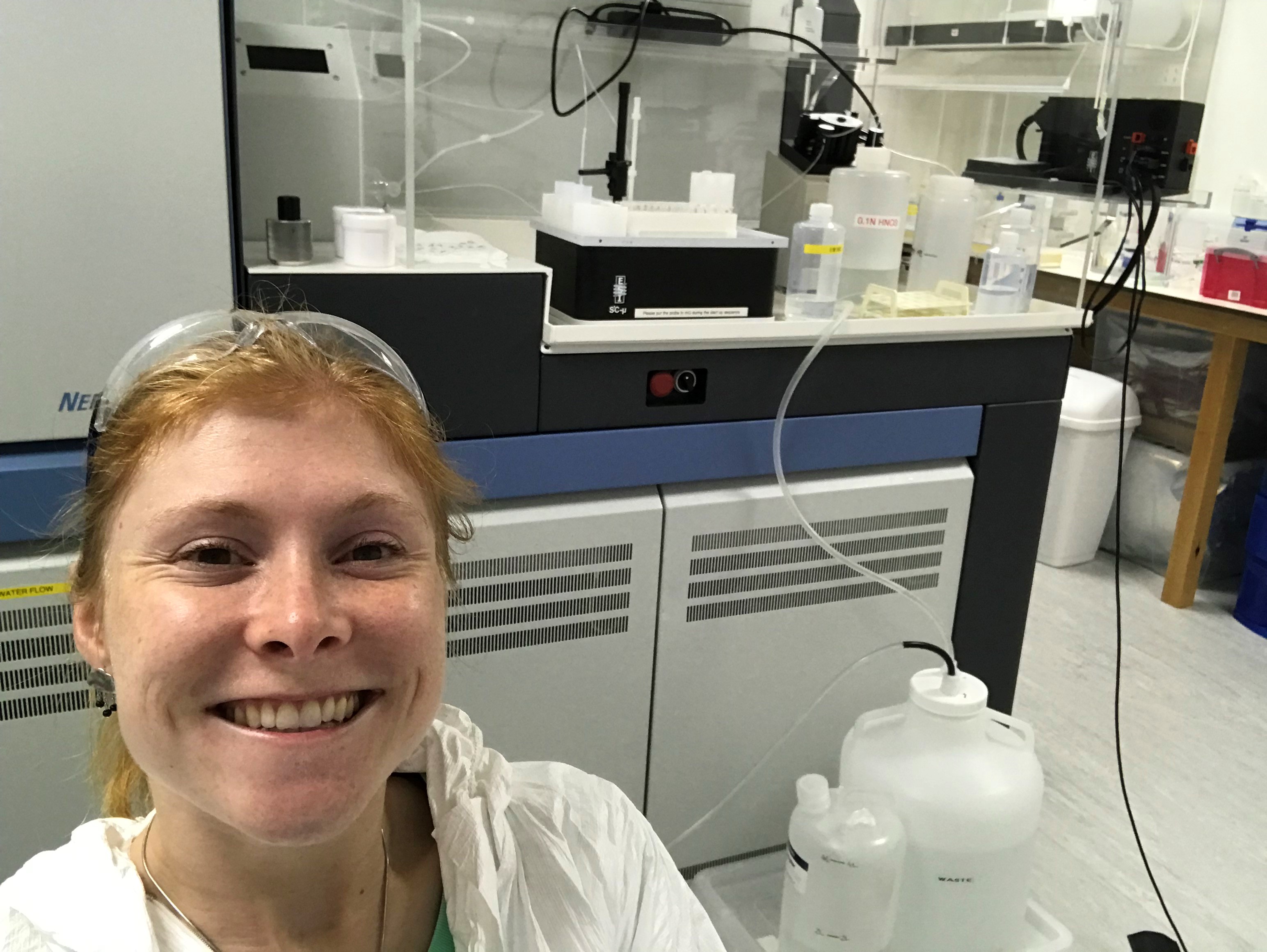 Carrie in the lab, wearing protective gear and stood in front of a mass spectrometer